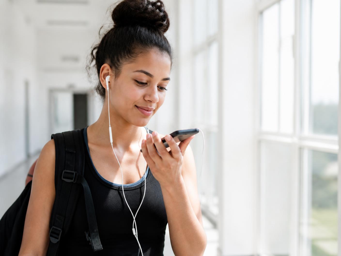 A teenage girl athlete listening to a voice message on her phone in a bright gym hallway