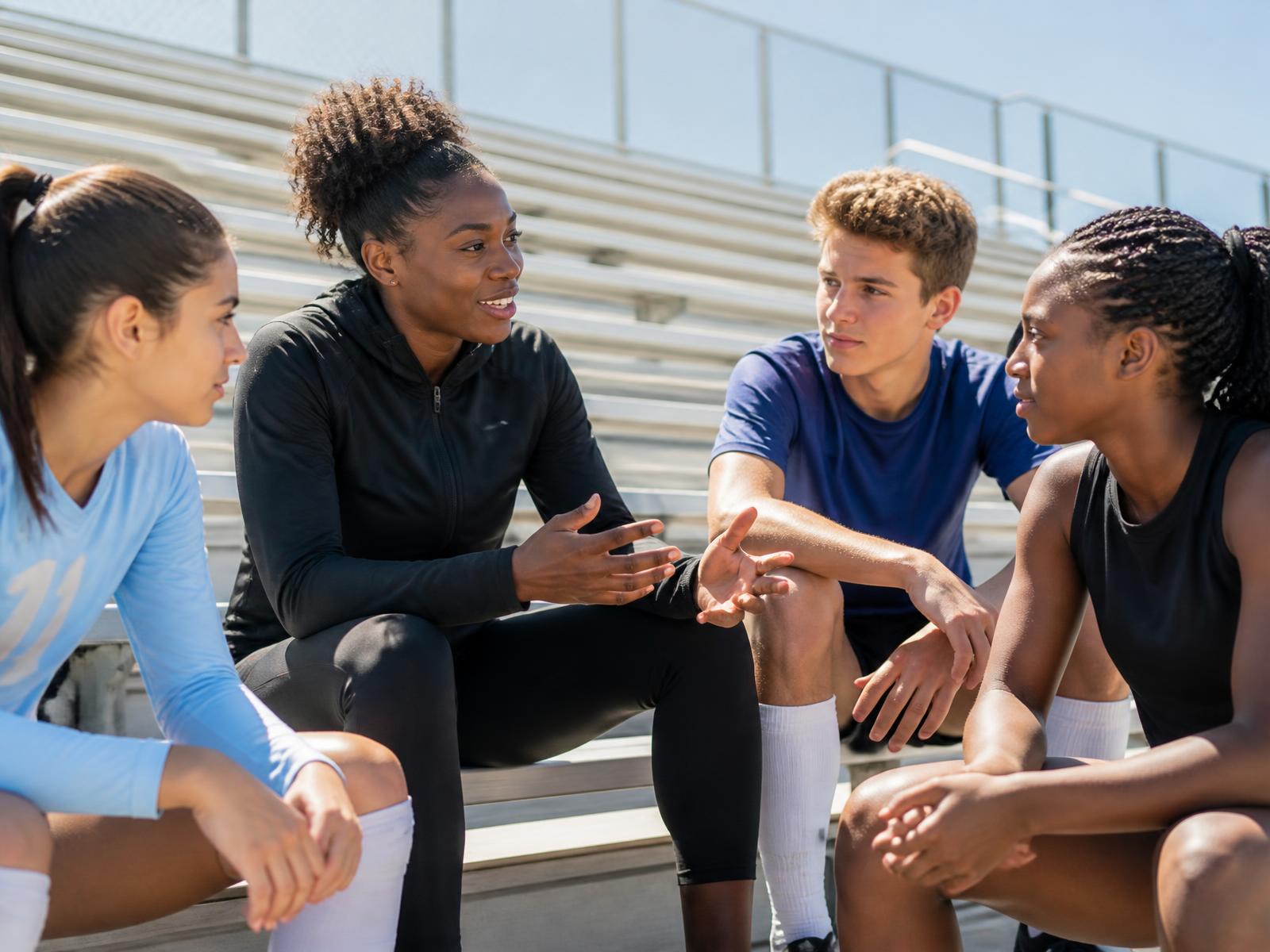 A professional track athlete sitting on sunlit bleachers in conversation with three teenage student-athletes
